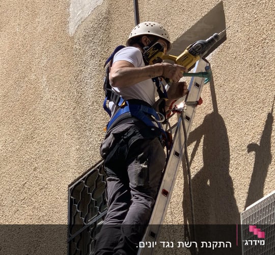 אדם על סולם עם מקדחה ליד פתח קיר
